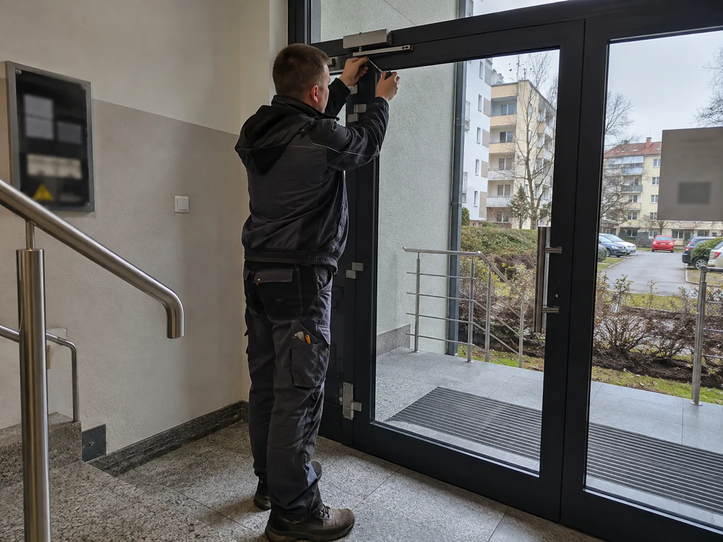 Technik pracuje przy samozamykaczu drzwi wejściowych